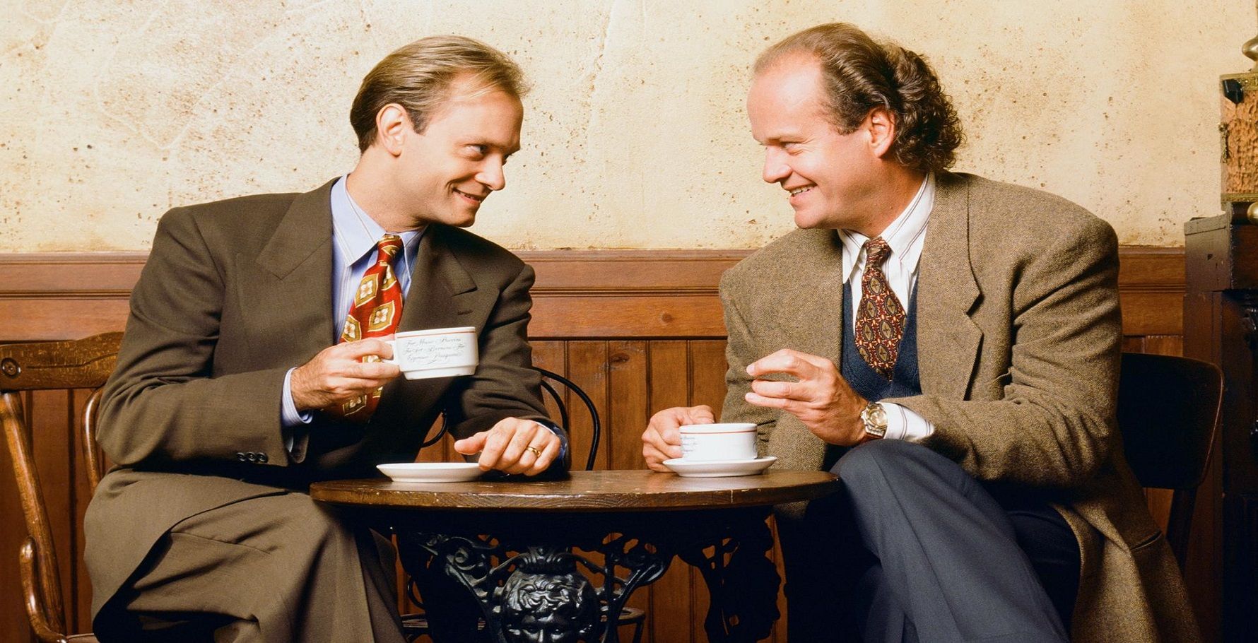 Niles and Frasier Crane sit across from each other at a cafe table drinking coffee.