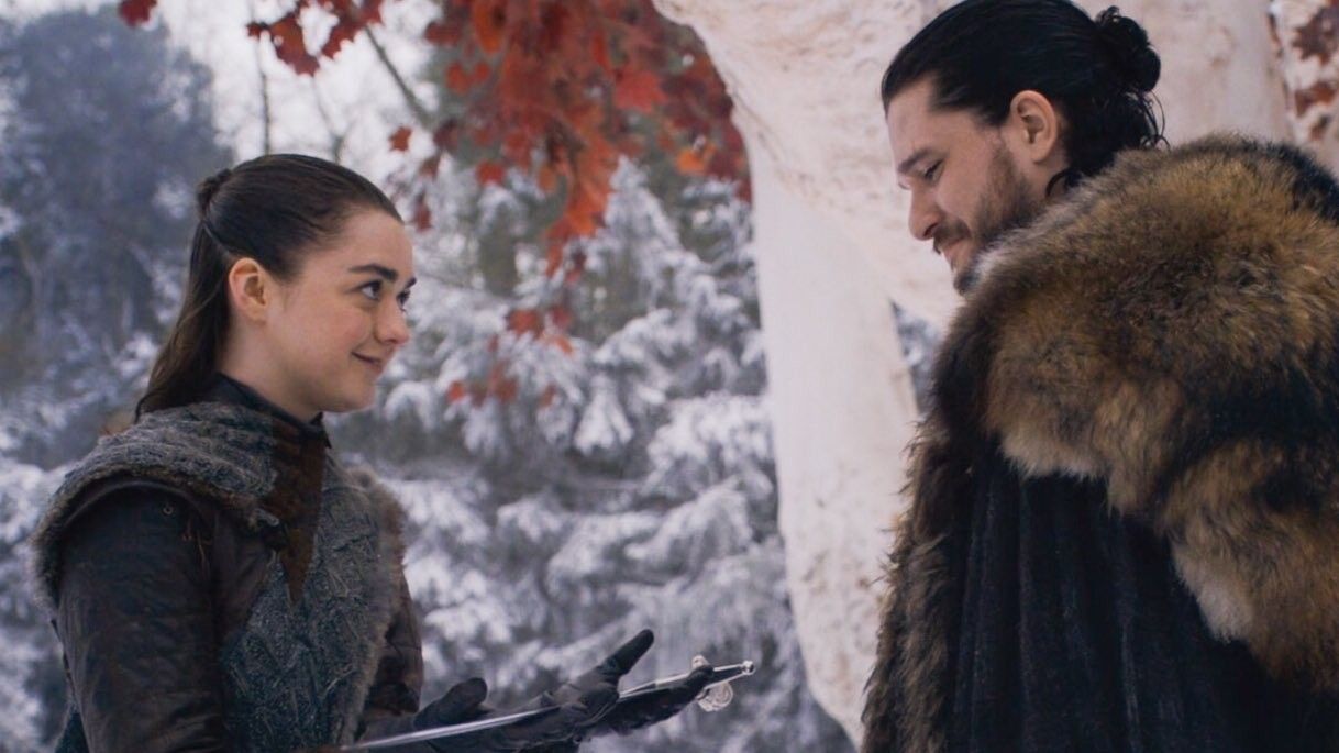 In a snowy forest, Arya holds out her sword to her brother Jon. 