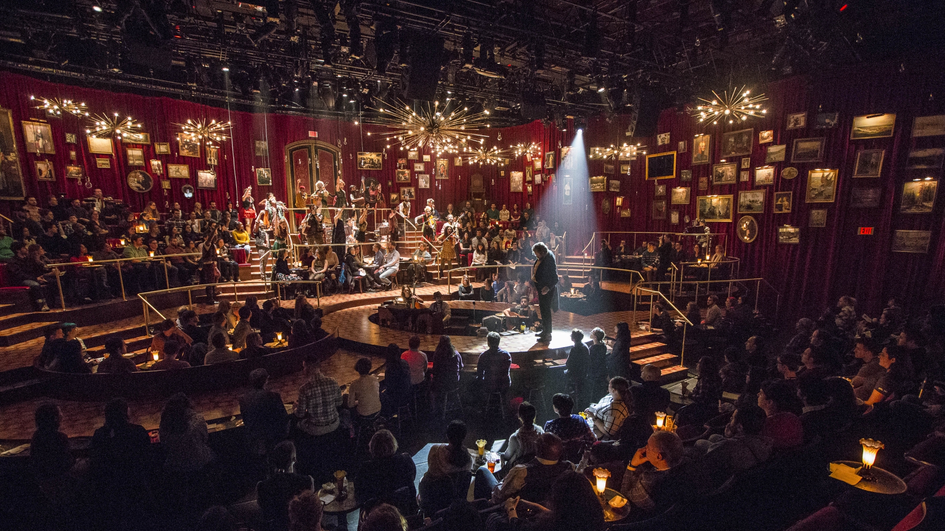 The audience sits all around and inside the stage as the spotlight shines on Pierre in a shot from a production of Natasha, Pierre, and the Great Comet of 1812, 2016-2017 (Photo by Gretjen Helene Photography).