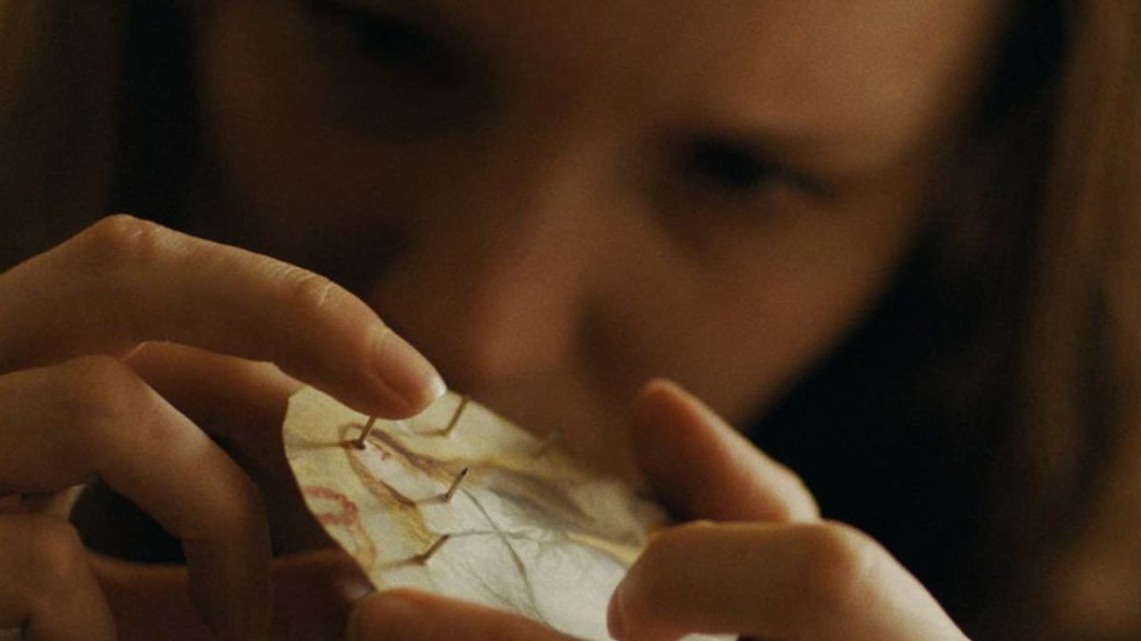 An close-up of Maud placing her finger on one of the pushpins that she's poked through her cut up card of Mary Magdalene