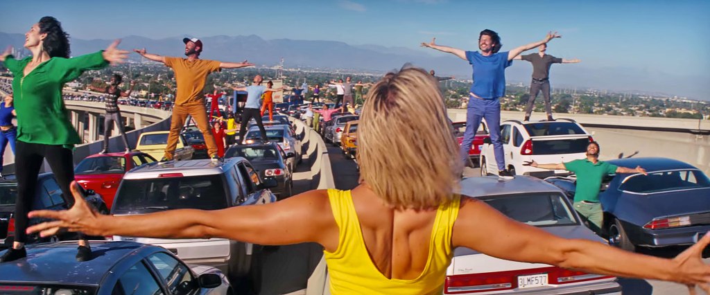 Joyful people singing and dancing on top of cars in traffic.