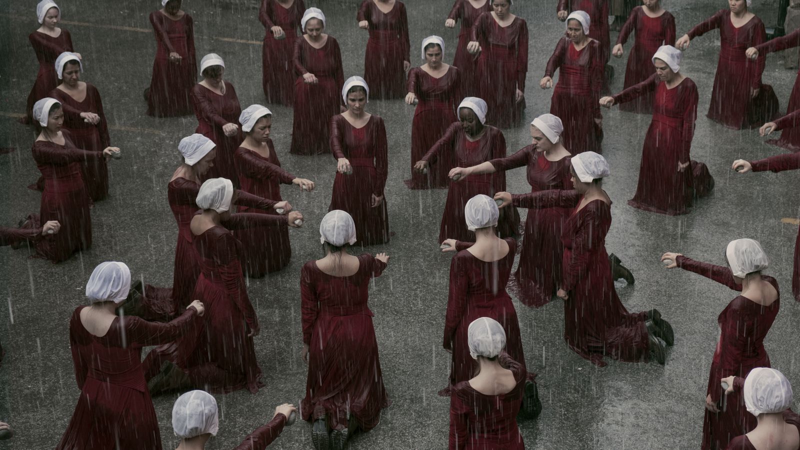 The handmaids kneeling outside in the rain, stones in hand.