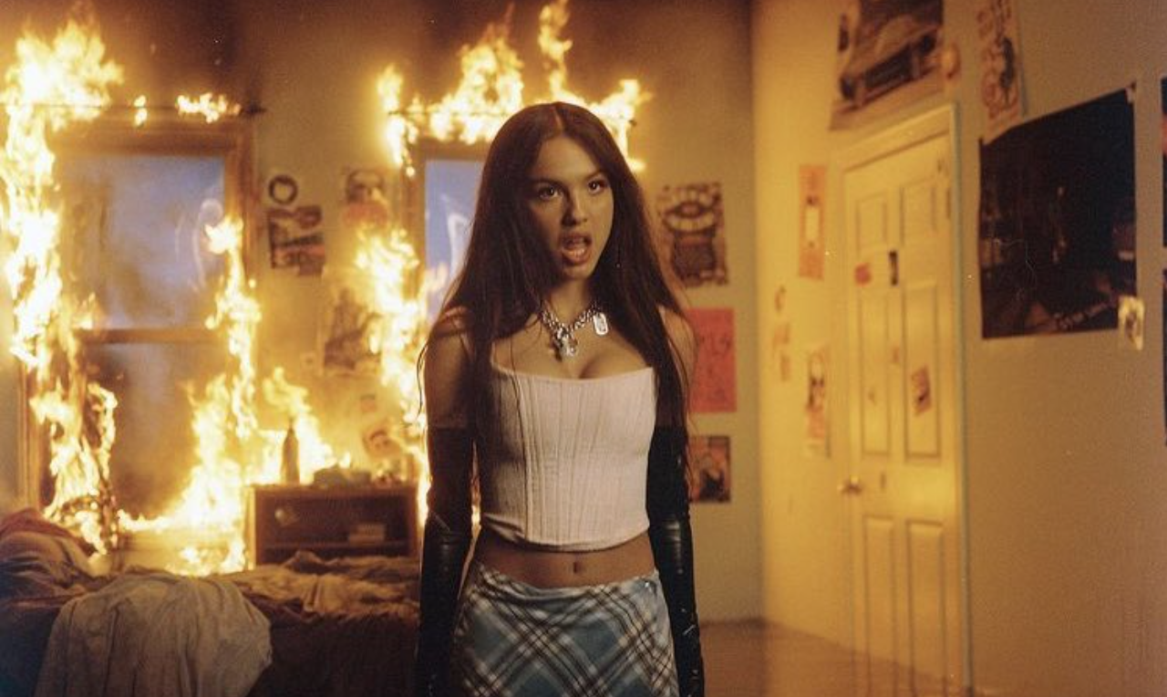 Olivia Rodrigo in her music video for her song, good 4 u. She is standing in a bedroom which is engulfed in flames.