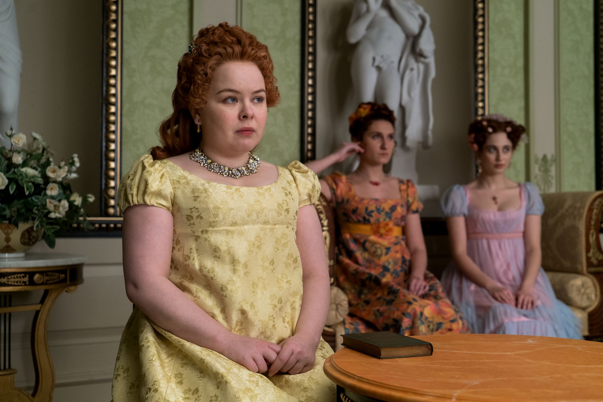 Penelope, Prudence, and Philippa Featherington all sit in the tea room (Penelope in the foreground) in Netflix's Bridgerton (2020-Present).