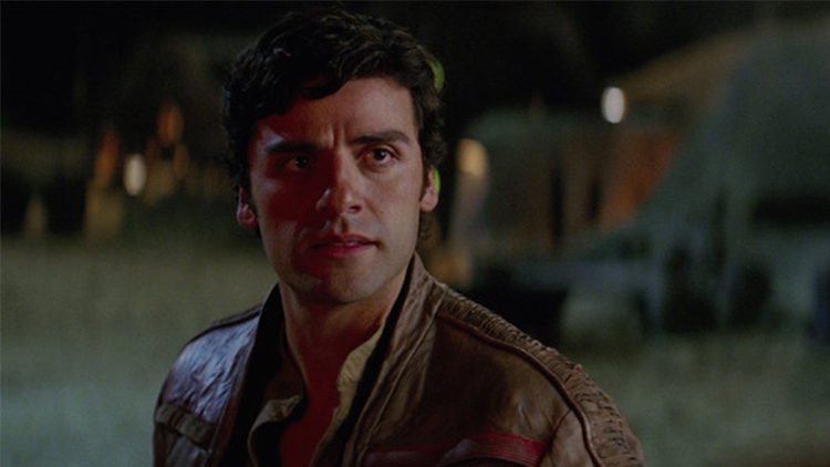 Oscar Isaac as Poe Dameron in the 2015 film Star Wars Ep 7, The Force Awakens. He is in front of stone buildings and holds his face in a neutral position.