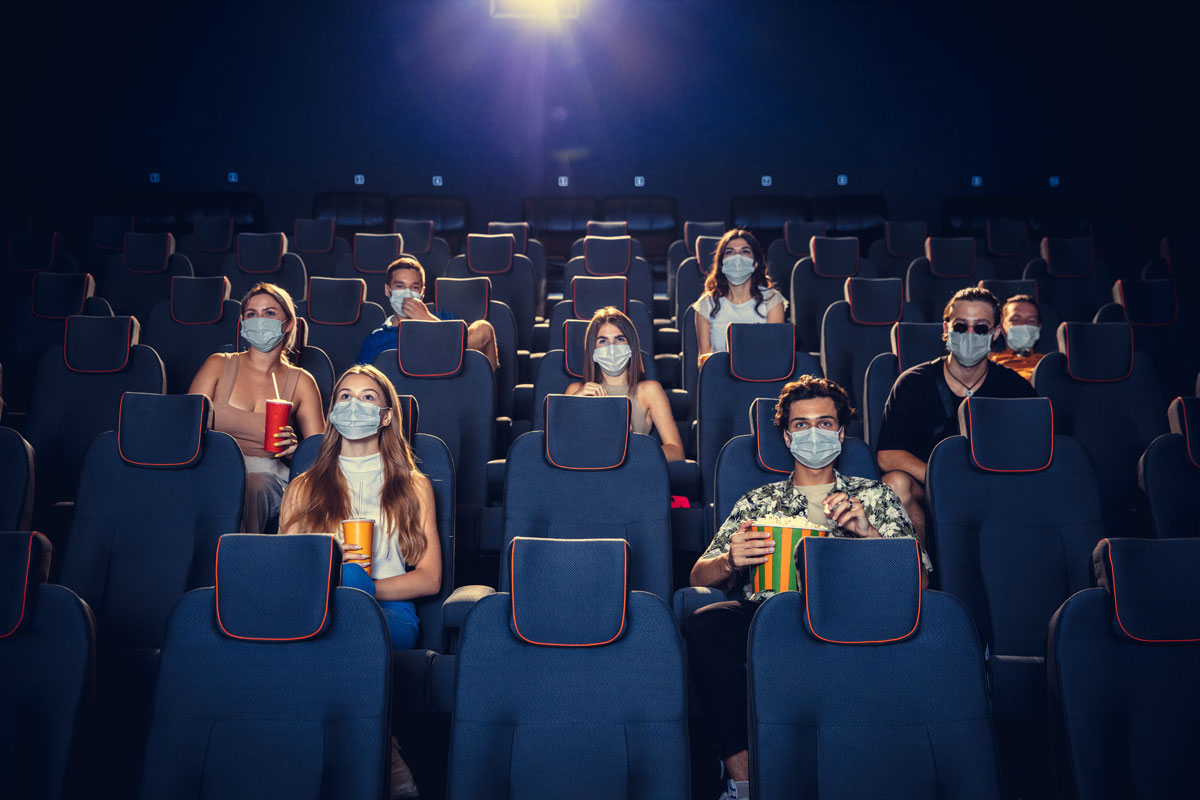 The crowd sits socially distanced and in masks at a movie theater. 