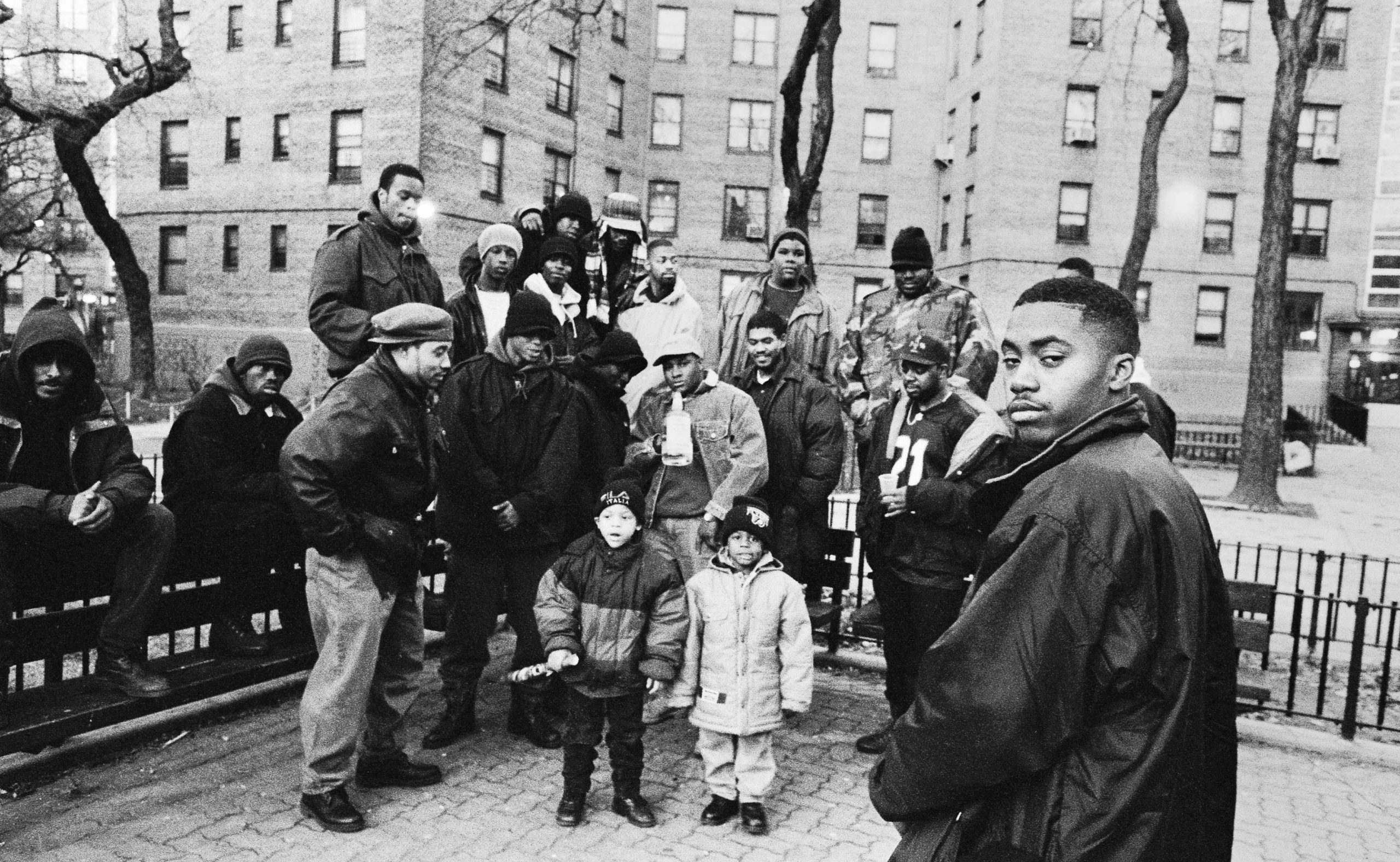 Nas poses in front of a group of people in the Queensbridge housing projects.