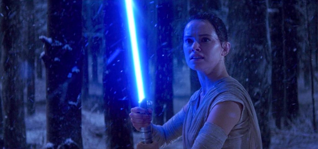 Daisy Ridley as Rey from Star Wars Episode 7: The Force Awakens. Half of her face is illuminated blue from a light saber. She has a scared and confused look on her face.