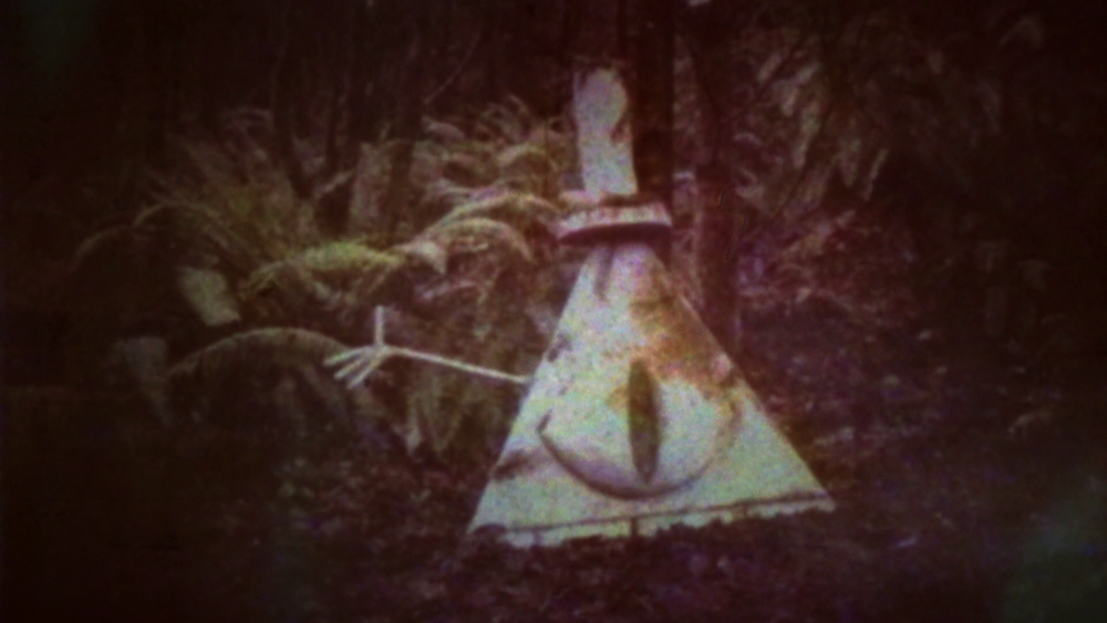 A grainy photograph of a statue of Bill Cipher in the woods. 