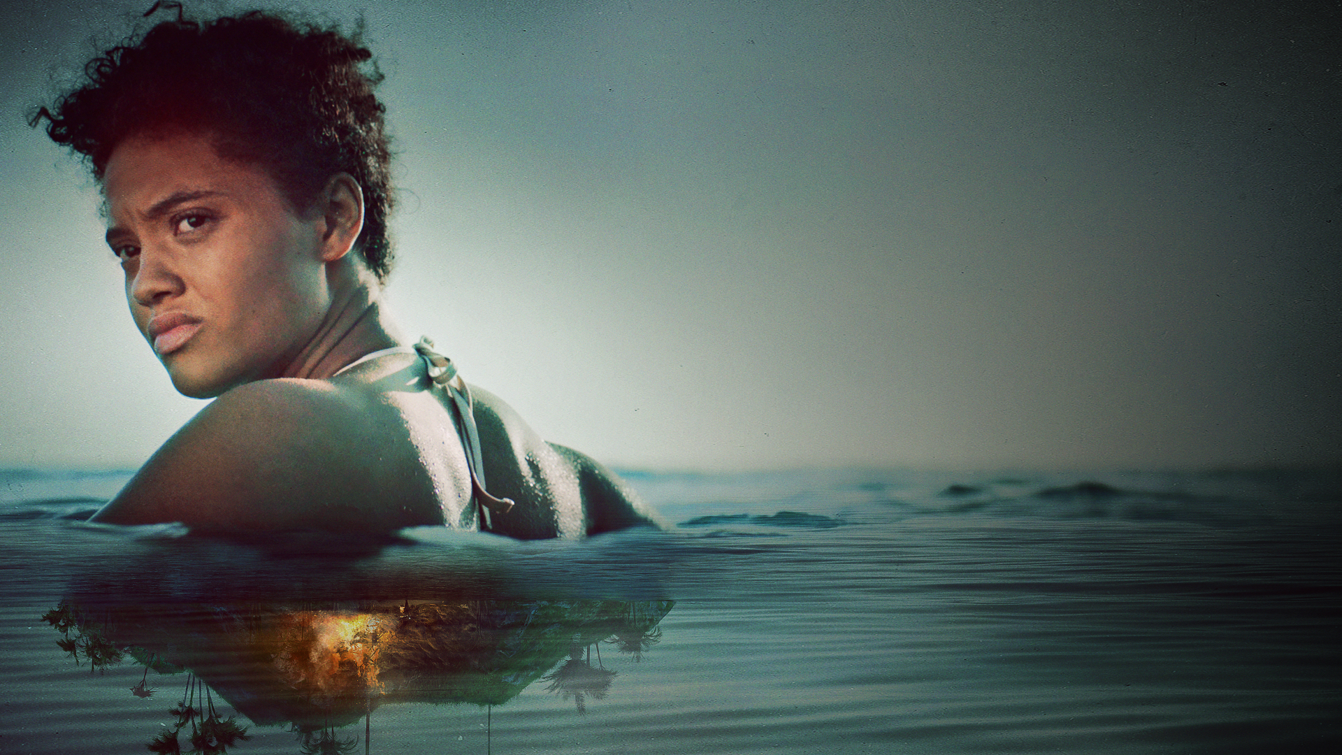 Kiersey Clemons as Jenn in Sweetheart. Jenn is in the water, looking back at the uninhabited island that is on fire.