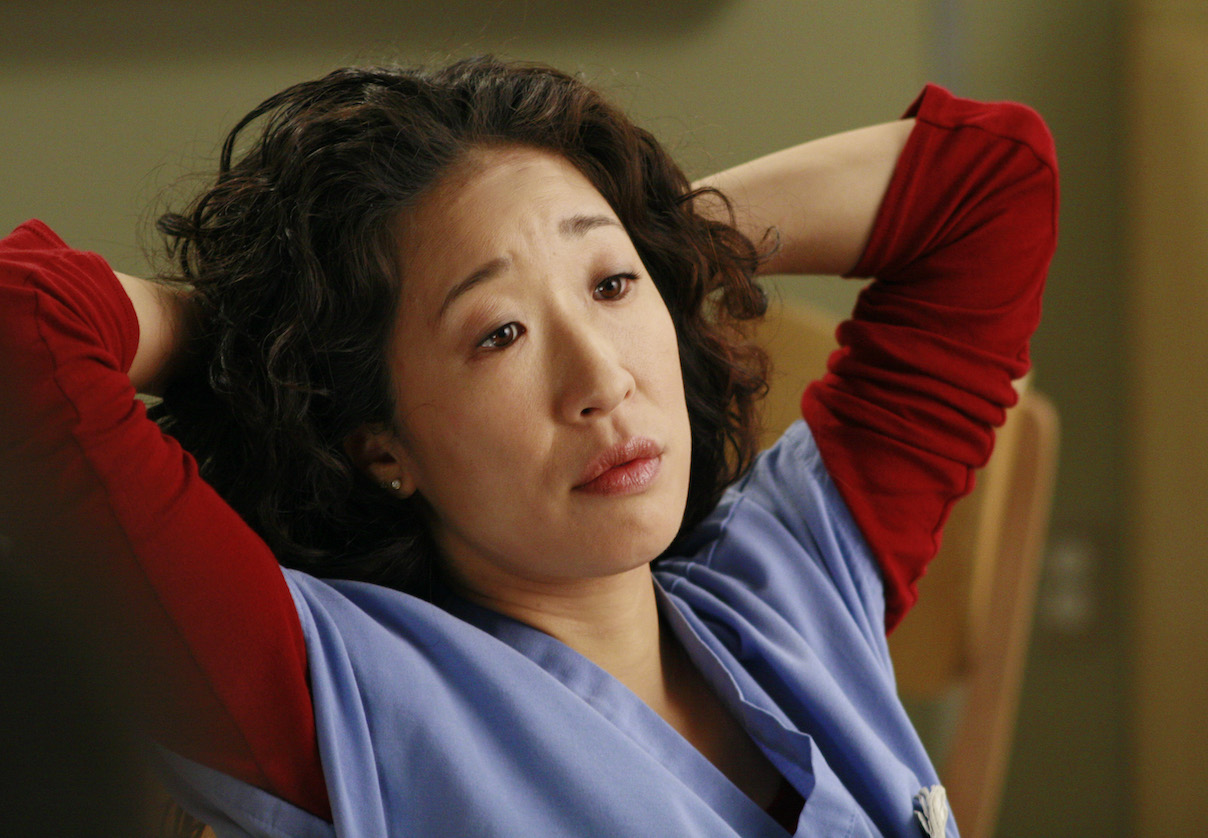 Cristina Yang leaning back in her chair with her arms behind her head in Grey's Anatomy (2005-Present).