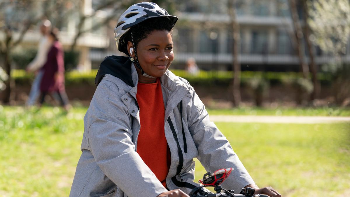 Dr. Sharon rides her bike outside while listening to music. She is smiling.