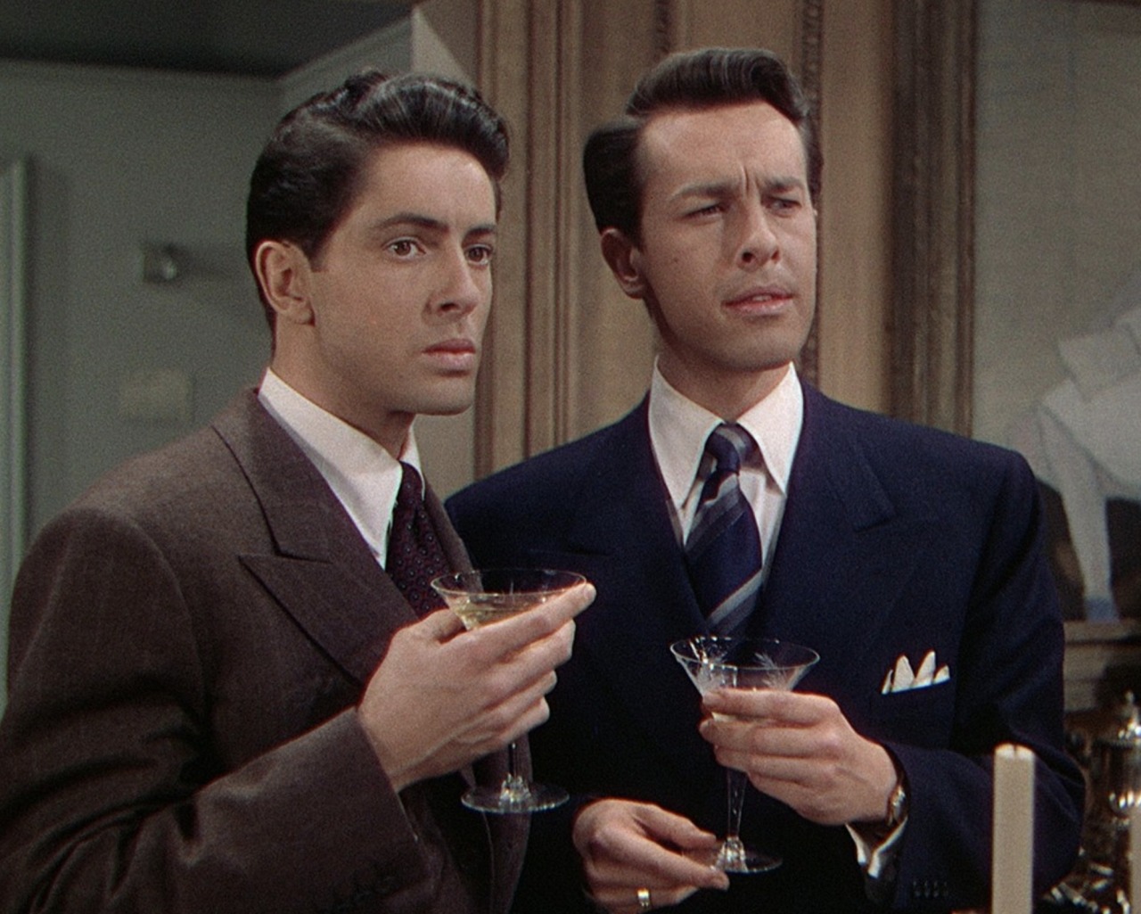 Phillip (Farley Granger) and Brandon Shaw (John Dall) are standing next to each other wearing suits and holding martini glasses.