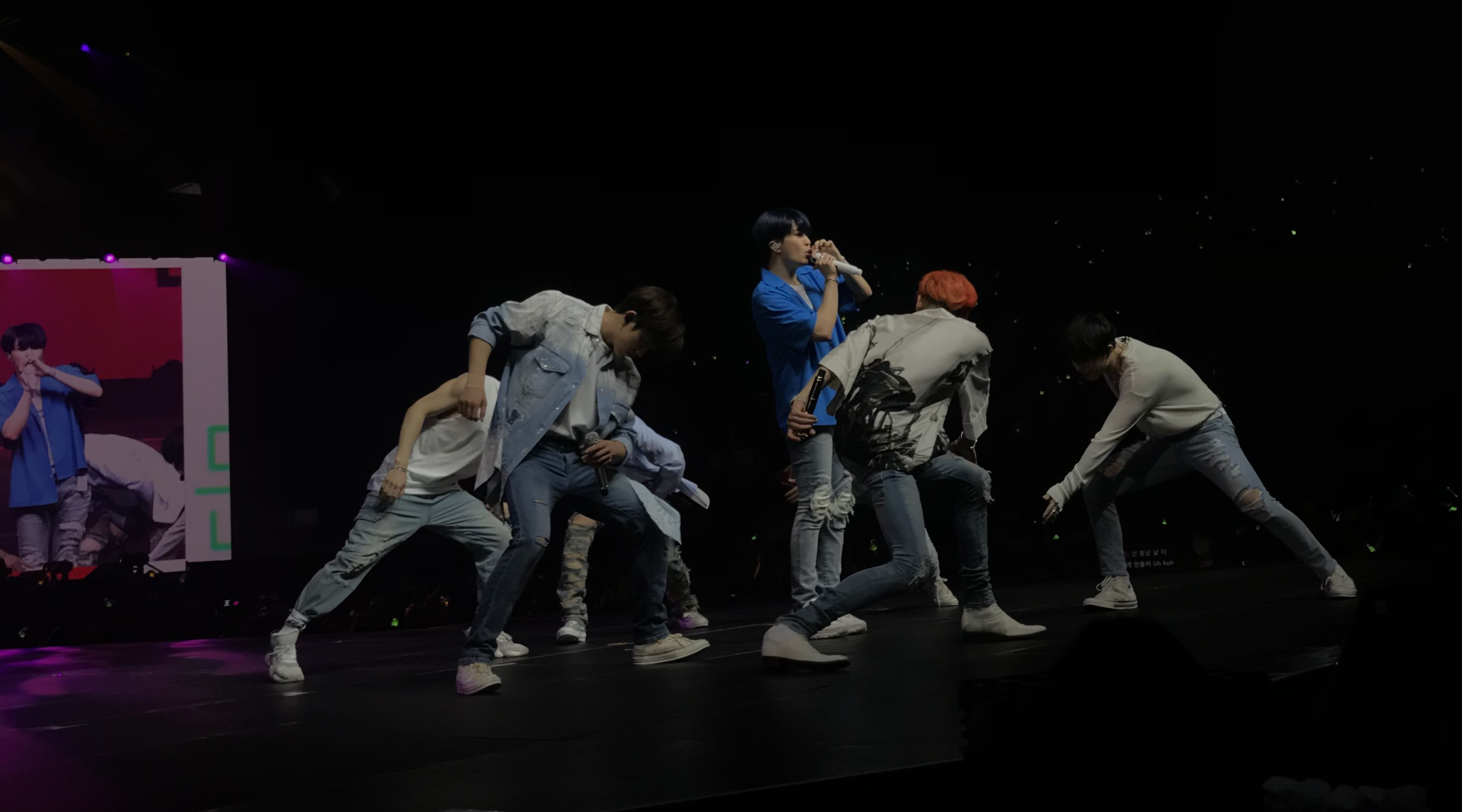 A fantaken image of Got7, the group of seven men are dancing with one member wearing a blue shirt centered in the middle while singing.