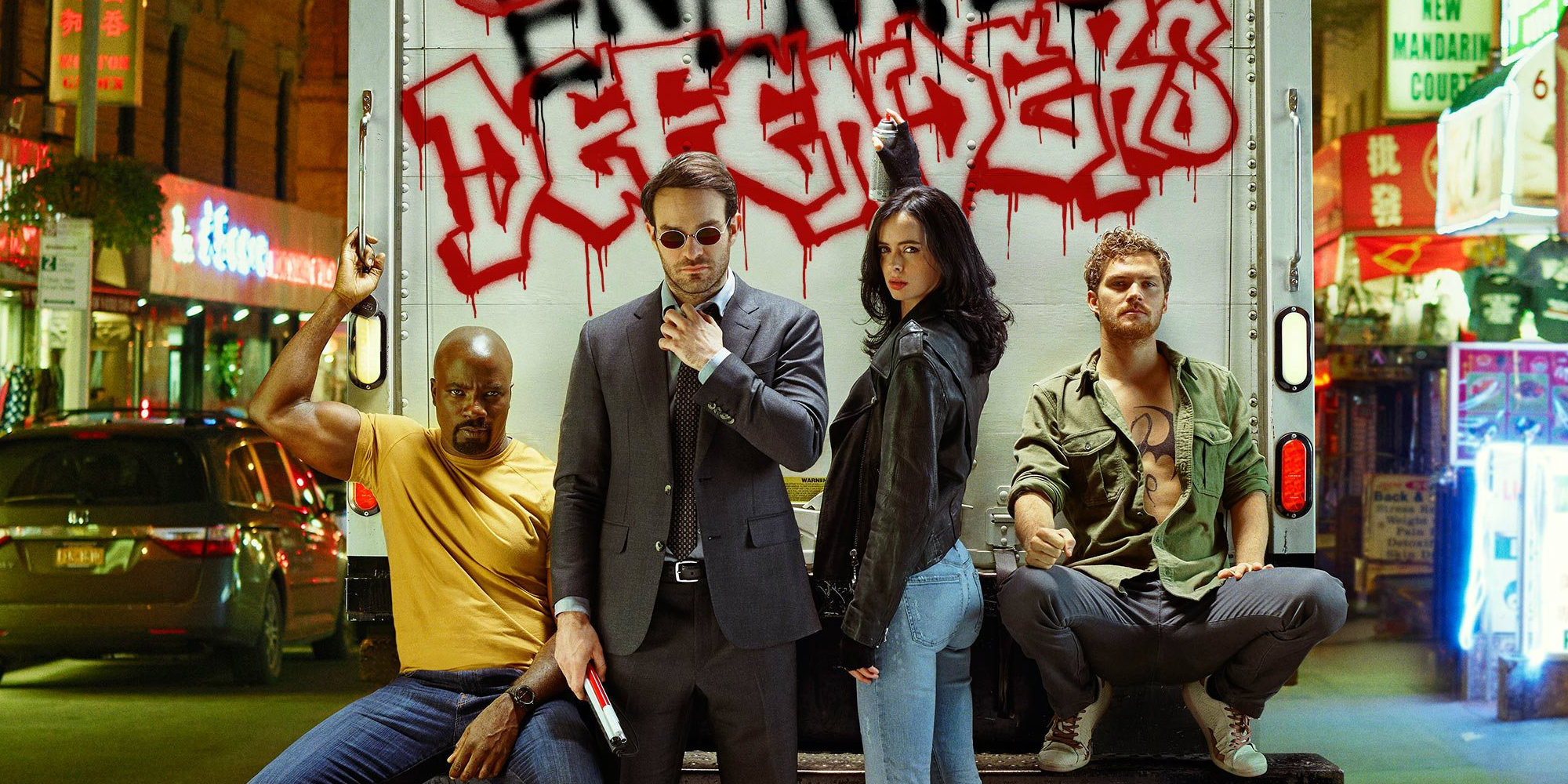 Luke Cage, Daredevil, Jessica Jones, and Iron Fist pose in front of a truck where Jessica has graffitied 'Defenders.'