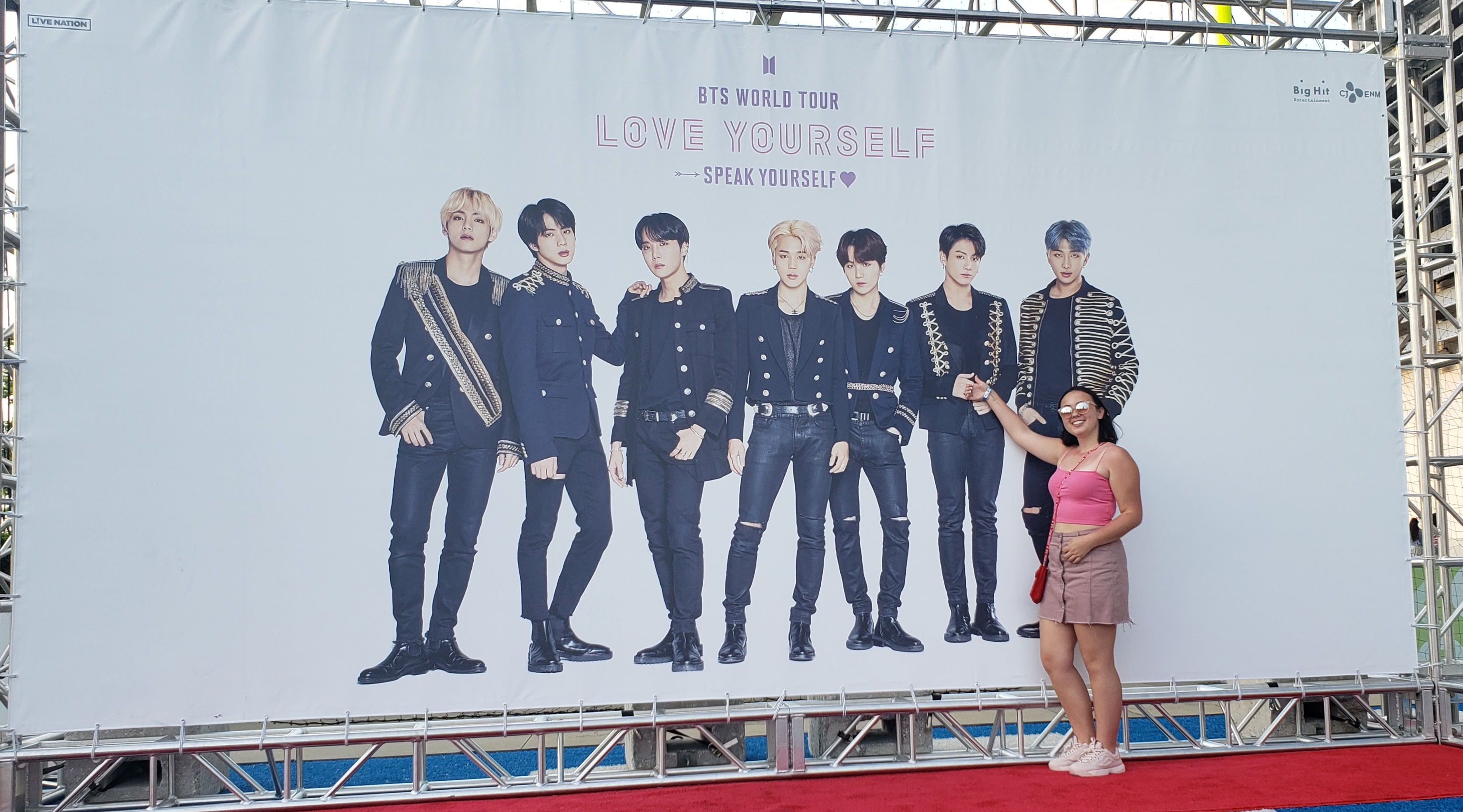 Marley Yu, an ARMY, taking photos at a BTS concert. She is wearing a pink crop top and a skirt while pointing up to BTS member Jungkook. 