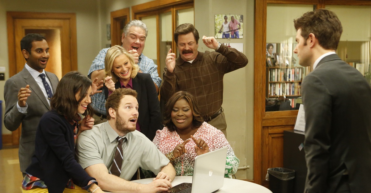 A group of people huddle around a computer. 