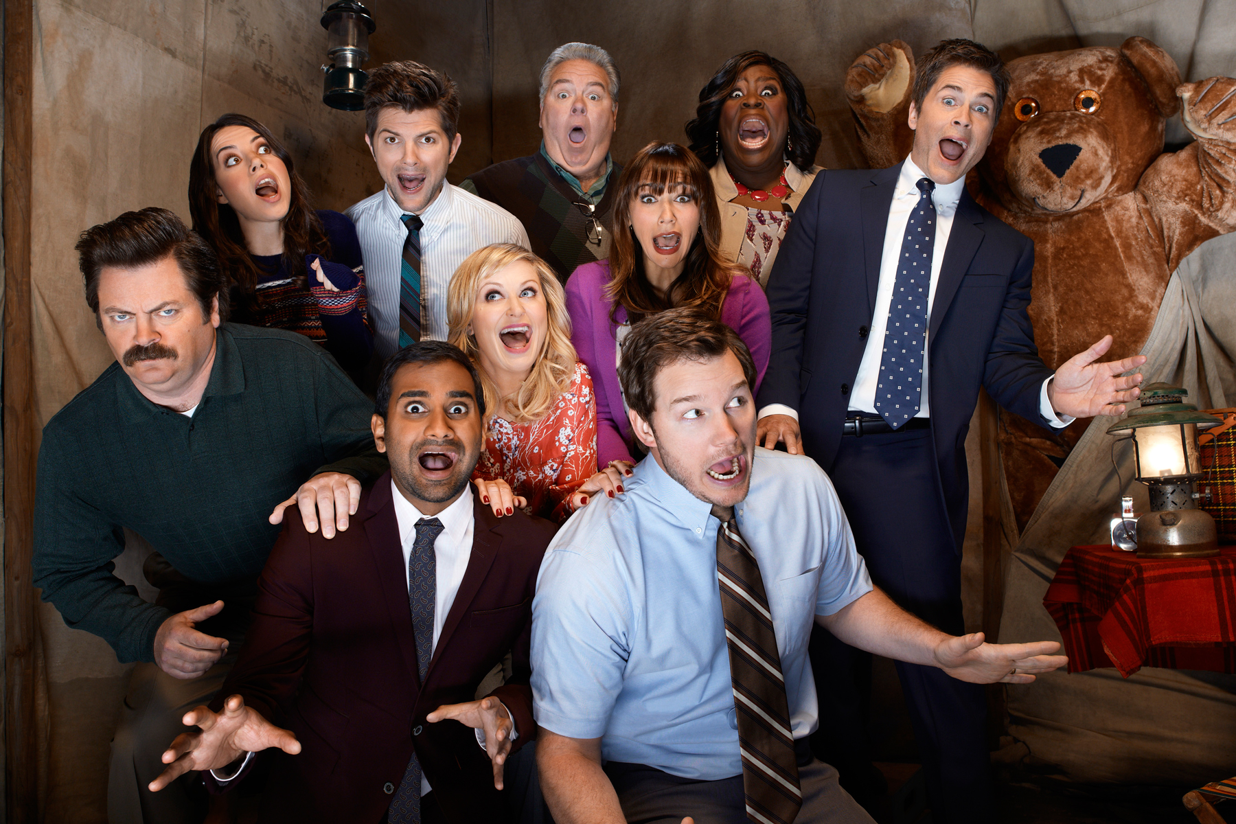 The cast of Parks and Recreation looking up at the camera as they make faces for a photo.