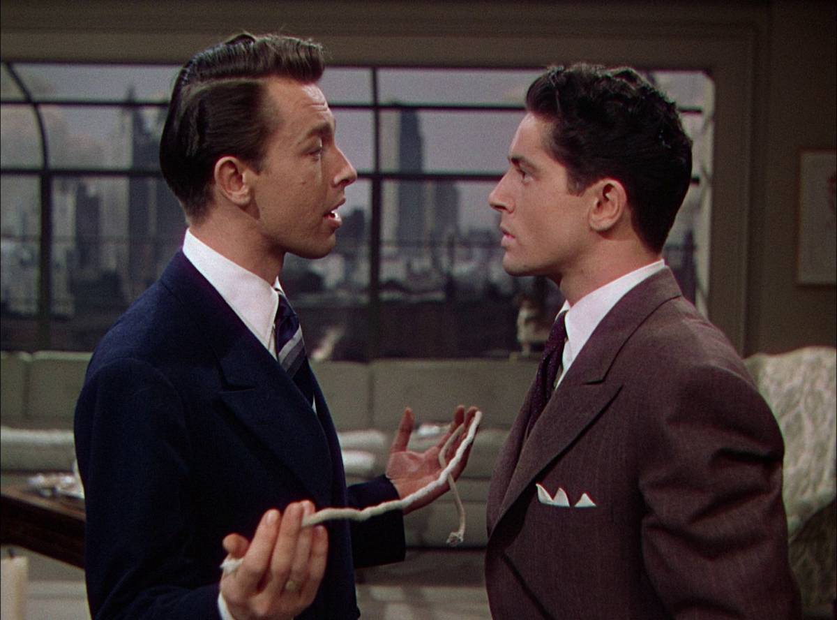 Brandon Shaw (John Dall) and Phillip (Farley Granger) are facing each other with Brandon holding a piece of rope.