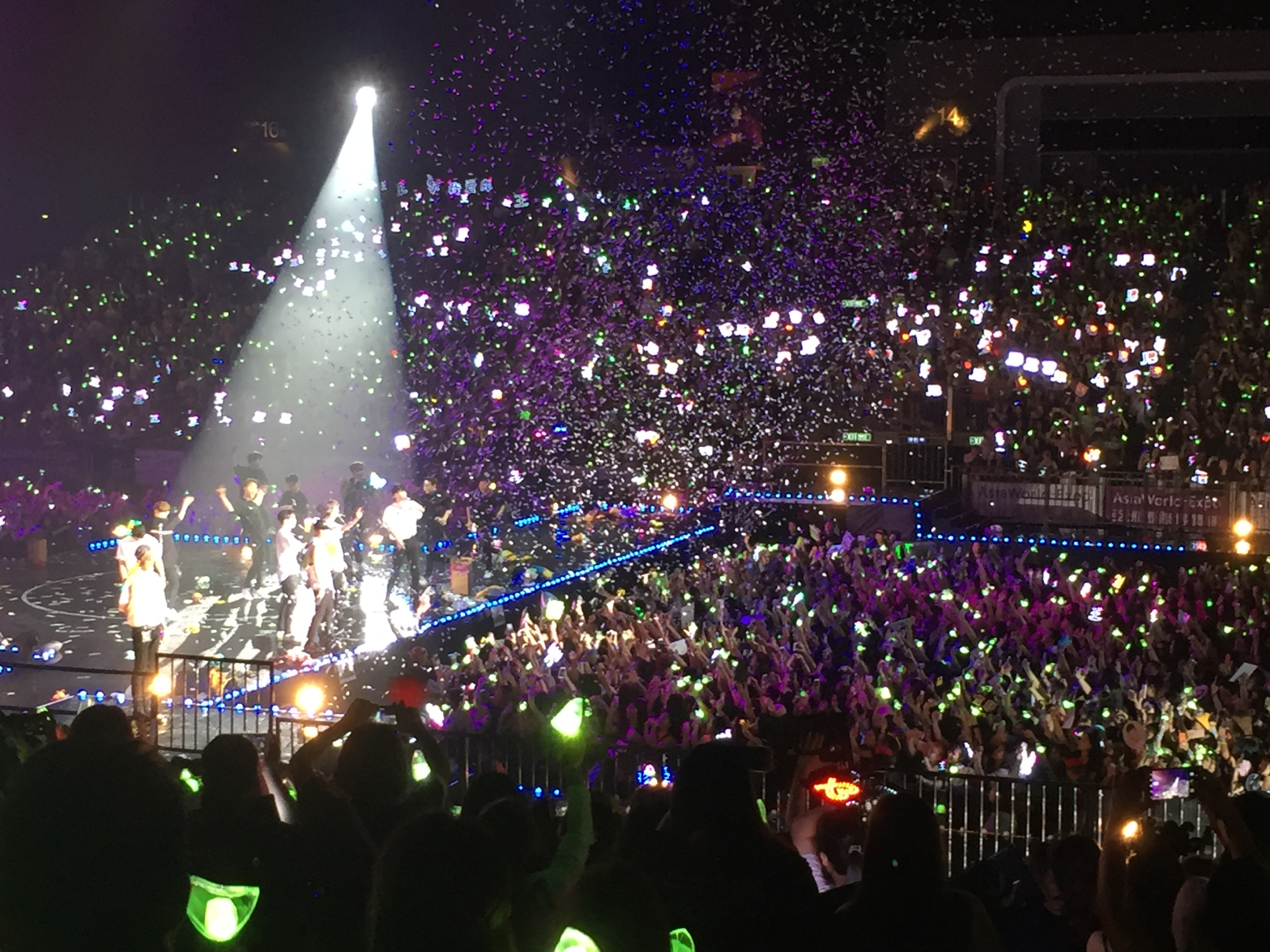 A stadium filled with fans and green lightsticks, a band stands in the middle with a spotlight on them.