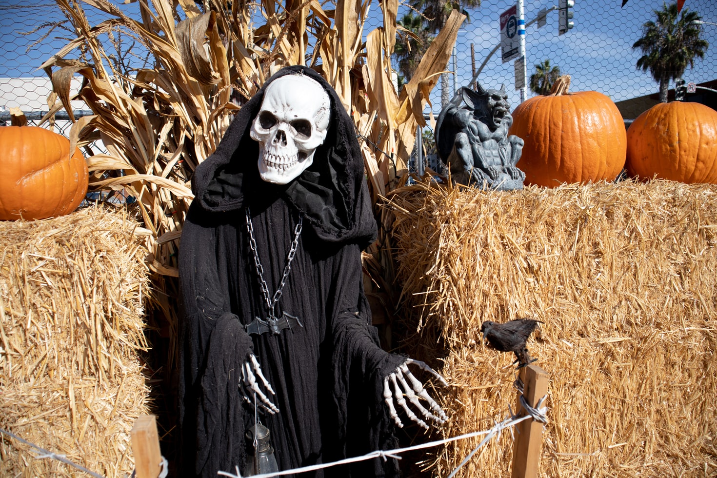 Skeleton in a hood between two stacks of hay that has orange pumpkins on top.