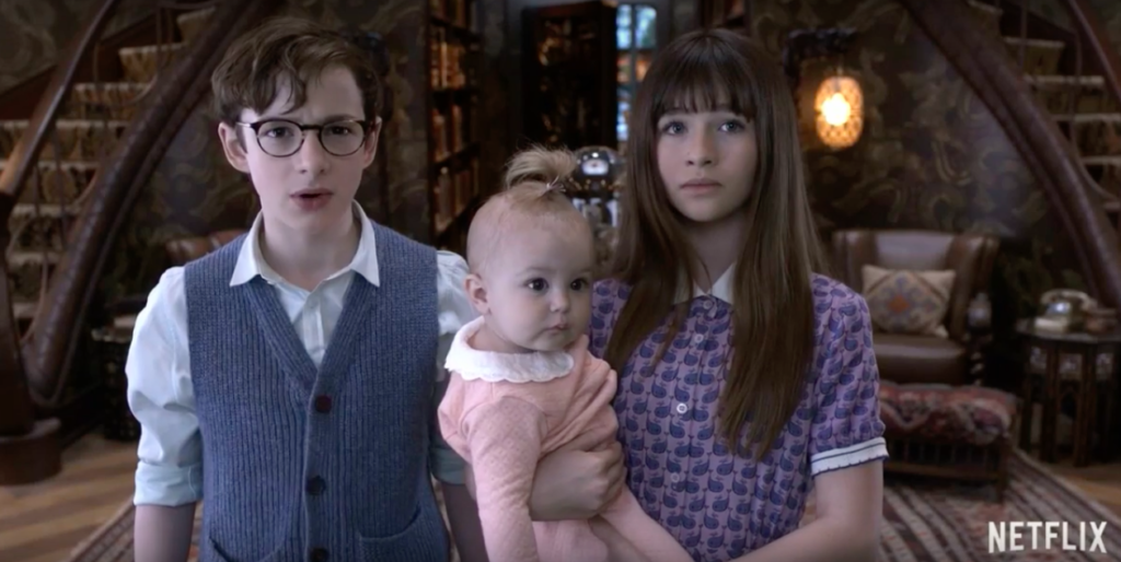 Klaus stands next to Violet while she holds Sunny in her arms. A Series of Unfortunate Events. Season 1, Episode 1: "The Bad Beginning: Part Two." 2017-2019. Netflix Entertainment.