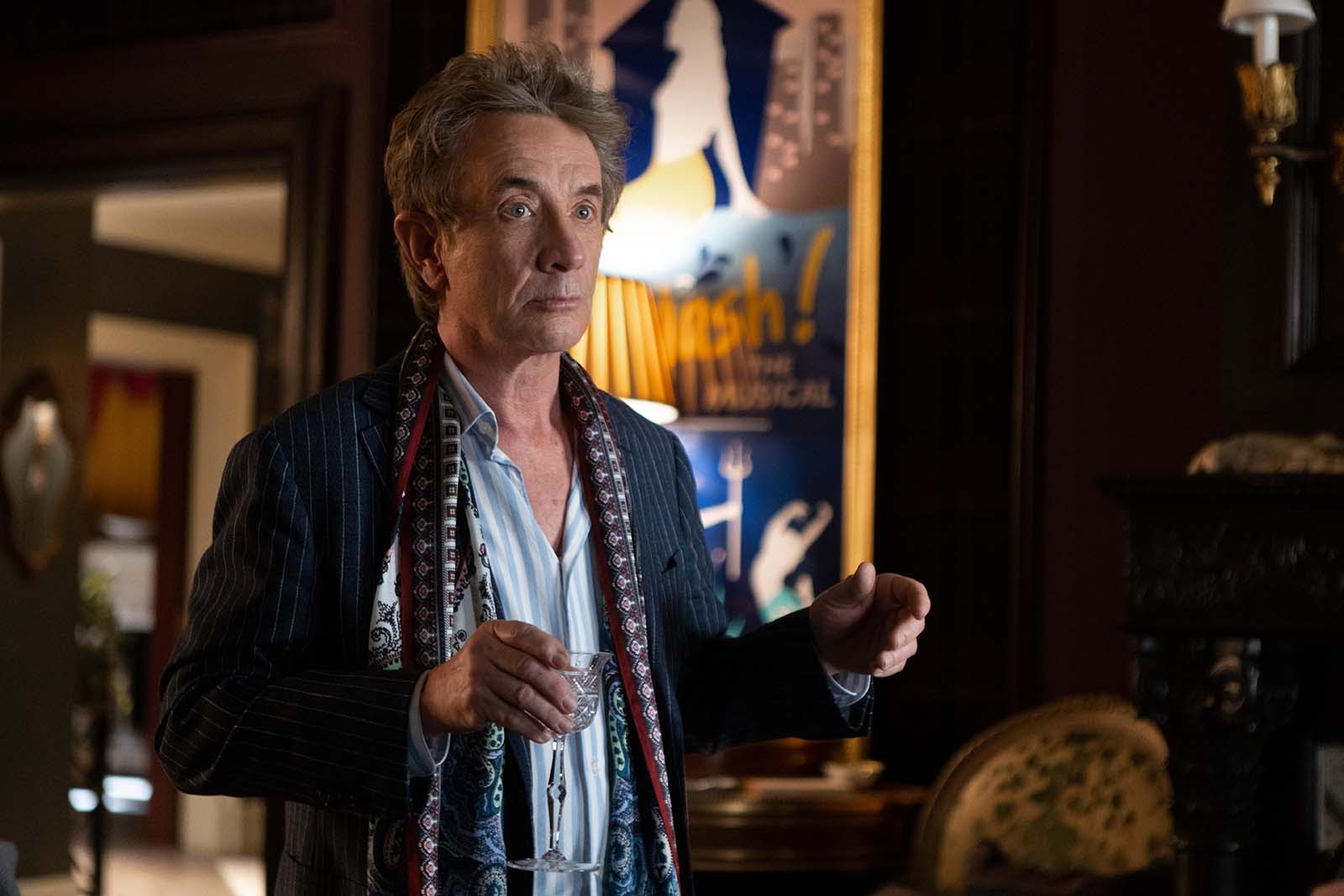 Oliver (Martin Short) is standing in his apartment holding a glass.