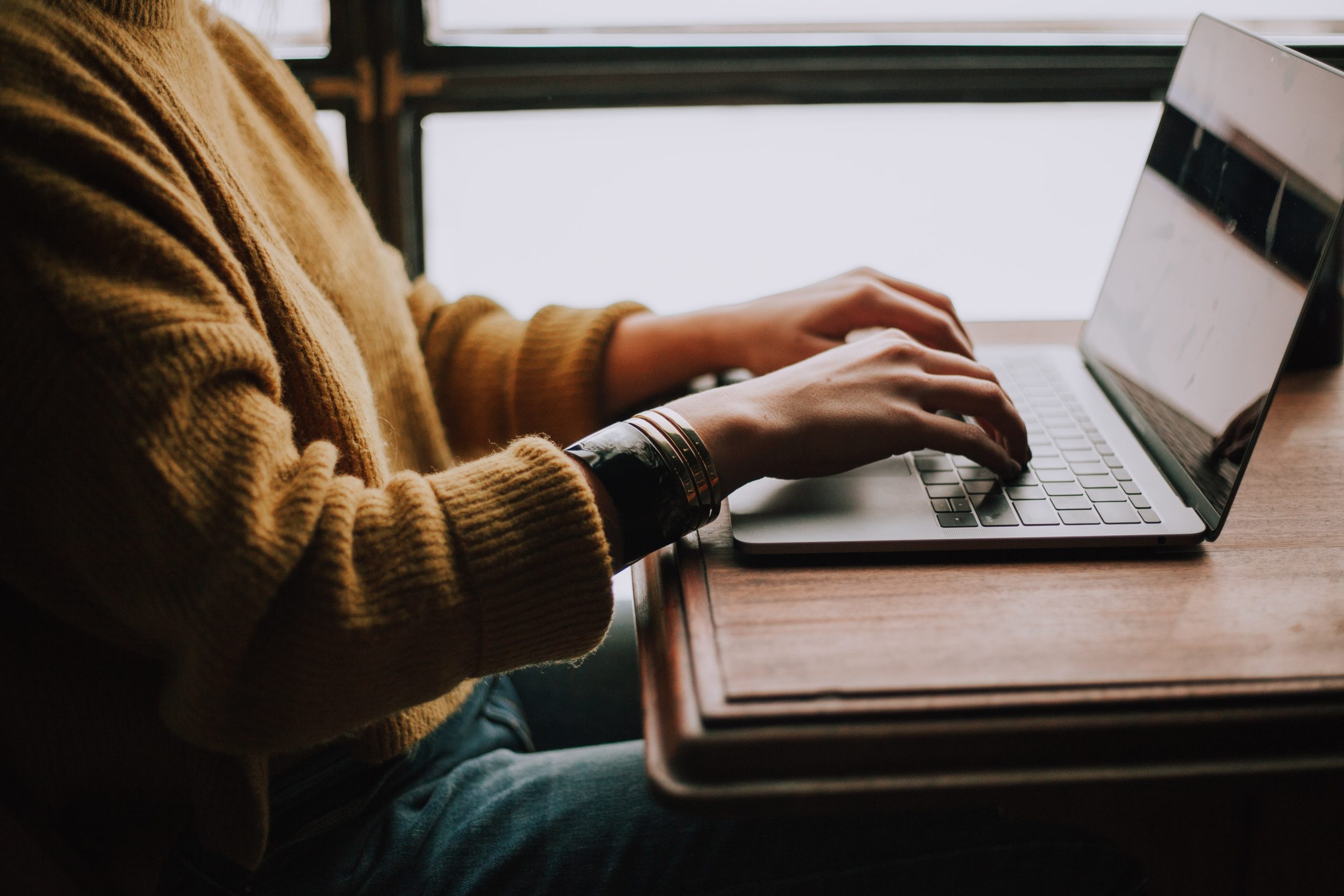 A person in a yellow sweater sitting at a laptop. Unsplash by christinhumephoto