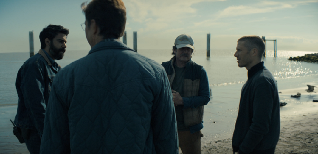 A group of islanders stand together in conversation on the shore of Crockett. Midnight Mass Season 1, Episode 2: "Book II: Psalms". 2021. Netflix Entertainment. 