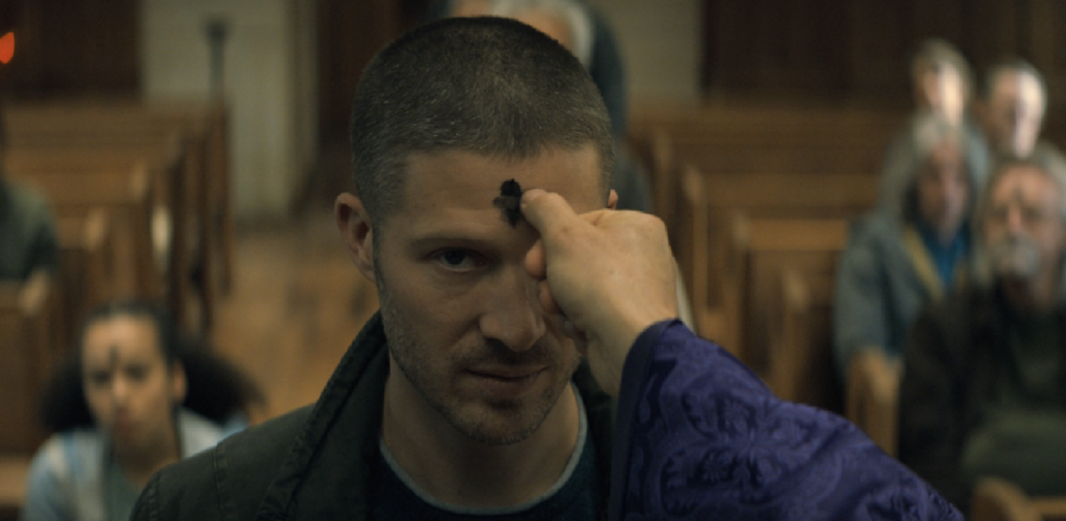 Father Paul marks an ash cross on Riley's head during Ash Wednesday mass. Midnight Mass. Season 1, Episode 2: "Book II: Psalms". 2021. Netflix Entertainment. 