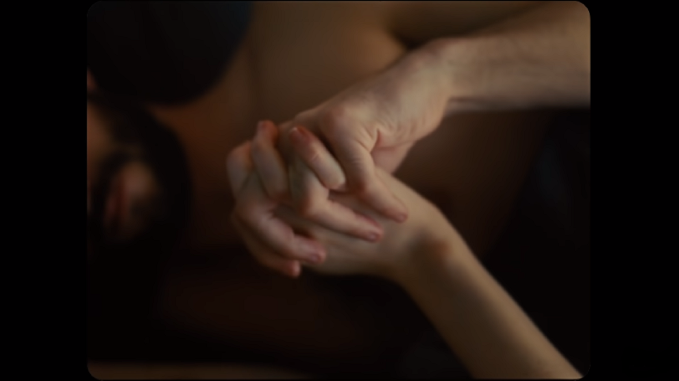 Sadie Sink and Dylan O'Brien's characters hold hands. The hands are centered, taking up the majority of the frame and the only part in focus.