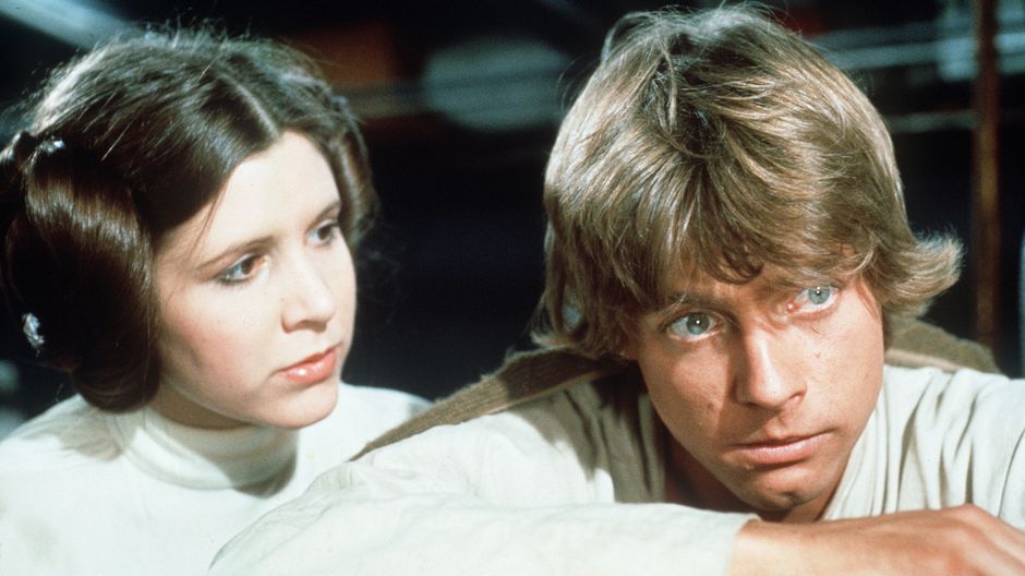 A still from Star Wars Episode IV, featuring Mark Hamill and Carrie Fisher. Fisher looks at Hamill who is looking at something off camera.