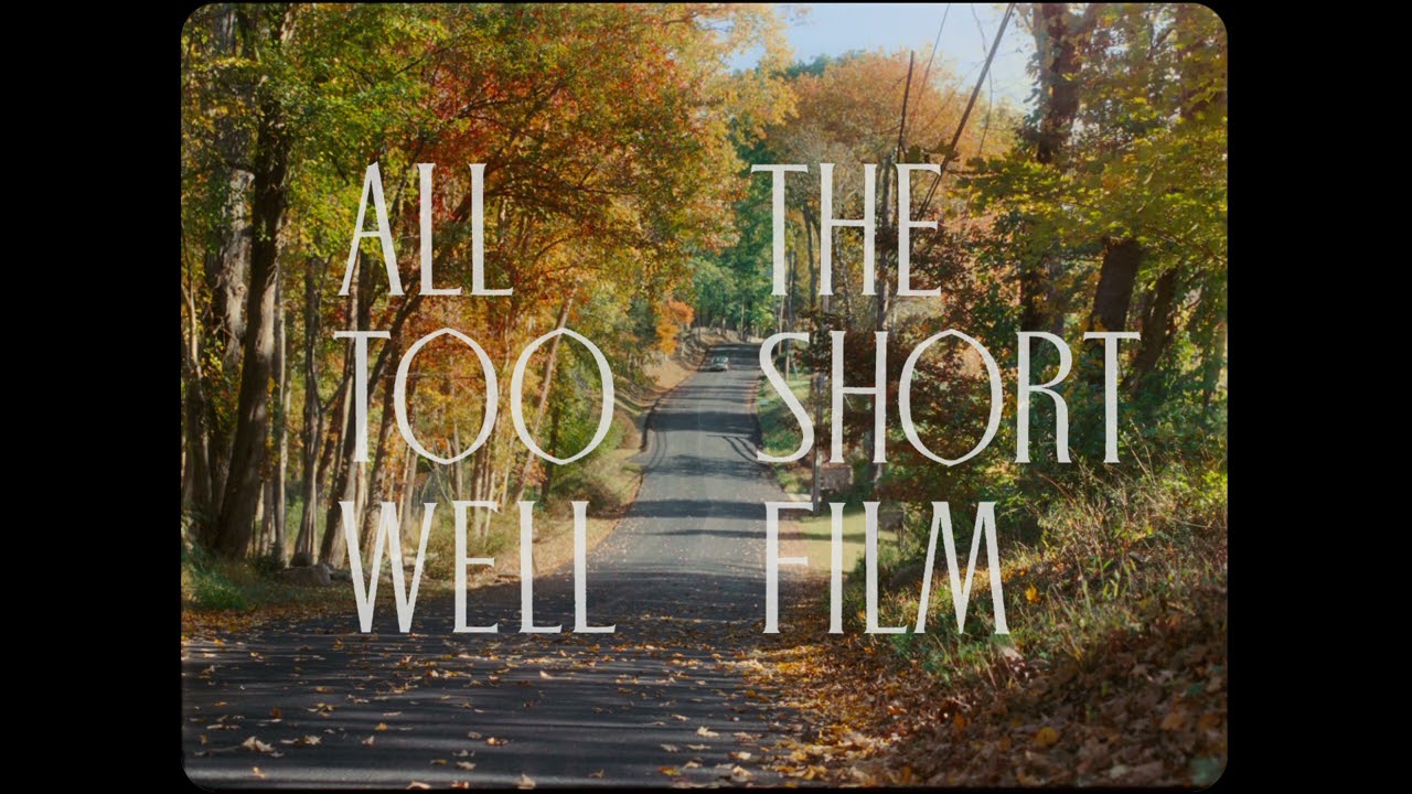 White text reading "All Too Well: The Short Film" over a colorful shot of autum trees on a long road. 