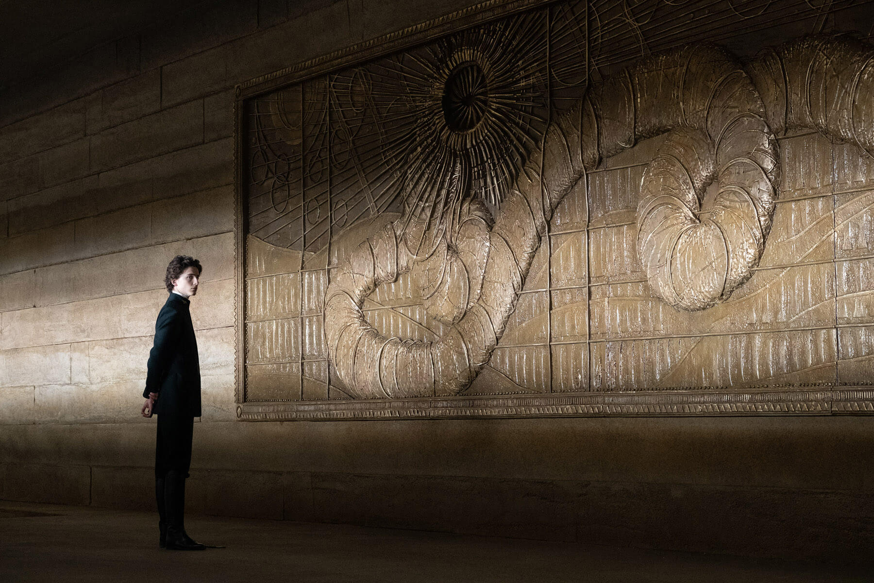 An image of Paul from the 2021 'Dune' looking at a mural of one of the sandworms. 