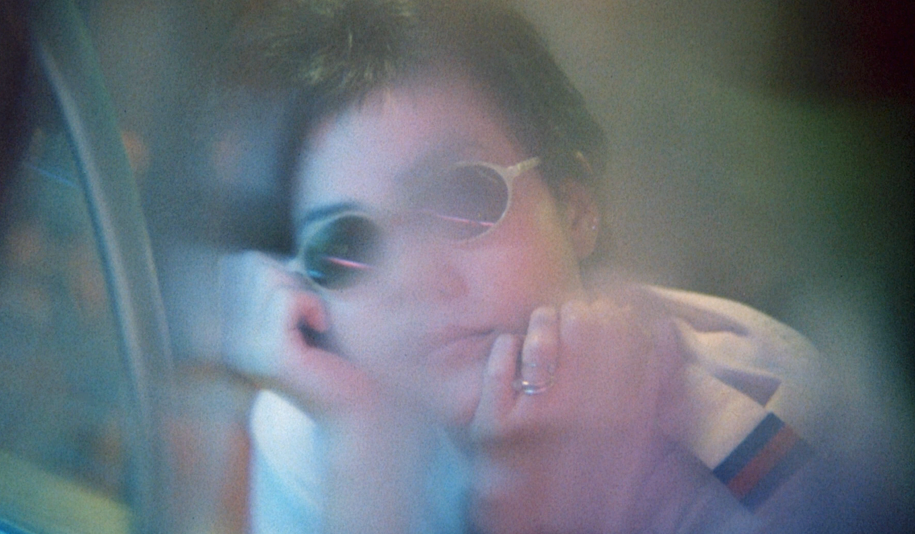 A film still from Chungking Express. This is a close-up of Faye Wong's character wearing sunglasses and gazing into the distance. It is hazy, dream-like. 