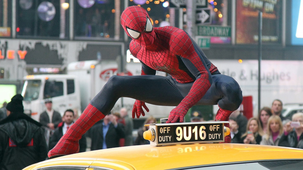 Spider-Man (Garfield) perches on top of a yellow taxi in New York City. 