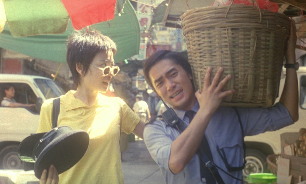 Faye and Cop 663 walk through a crowded Hong Kong street. He carries a basket of supplies for her. 