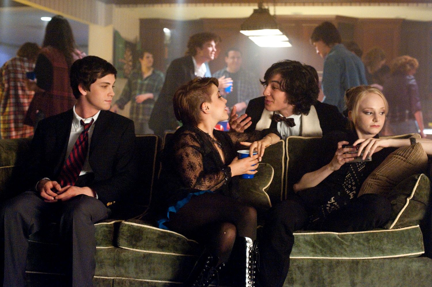 Charlie sits on the couch to the left of Patrick, Mary Elizabeth, and, Alice, unincluded in the conversation, in 'The Perks of Being a Wallflower' (2012).