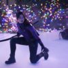 Kate Bishop from the series "Hawkeye" kneels on an ice rink holding a bow. She has one knee down and is looking to her left..