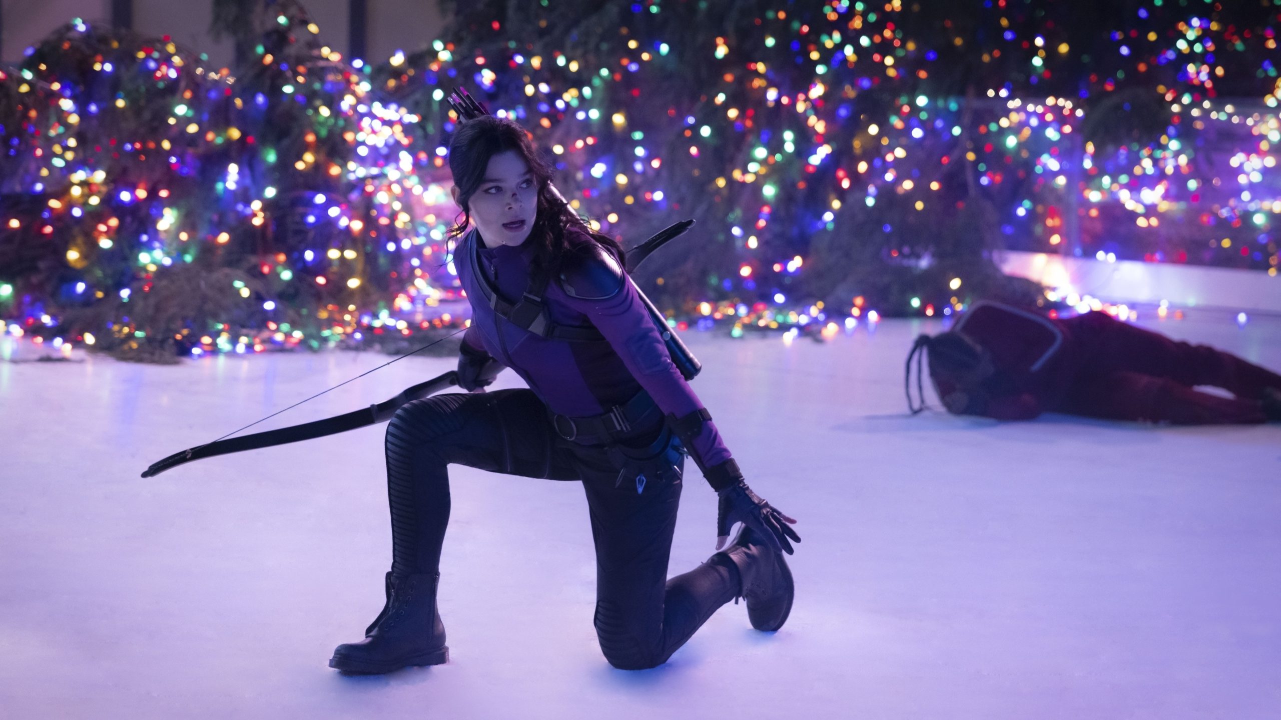 Kate Bishop from the series "Hawkeye" kneels on an ice rink holding a bow. She has one knee down and is looking to her left..