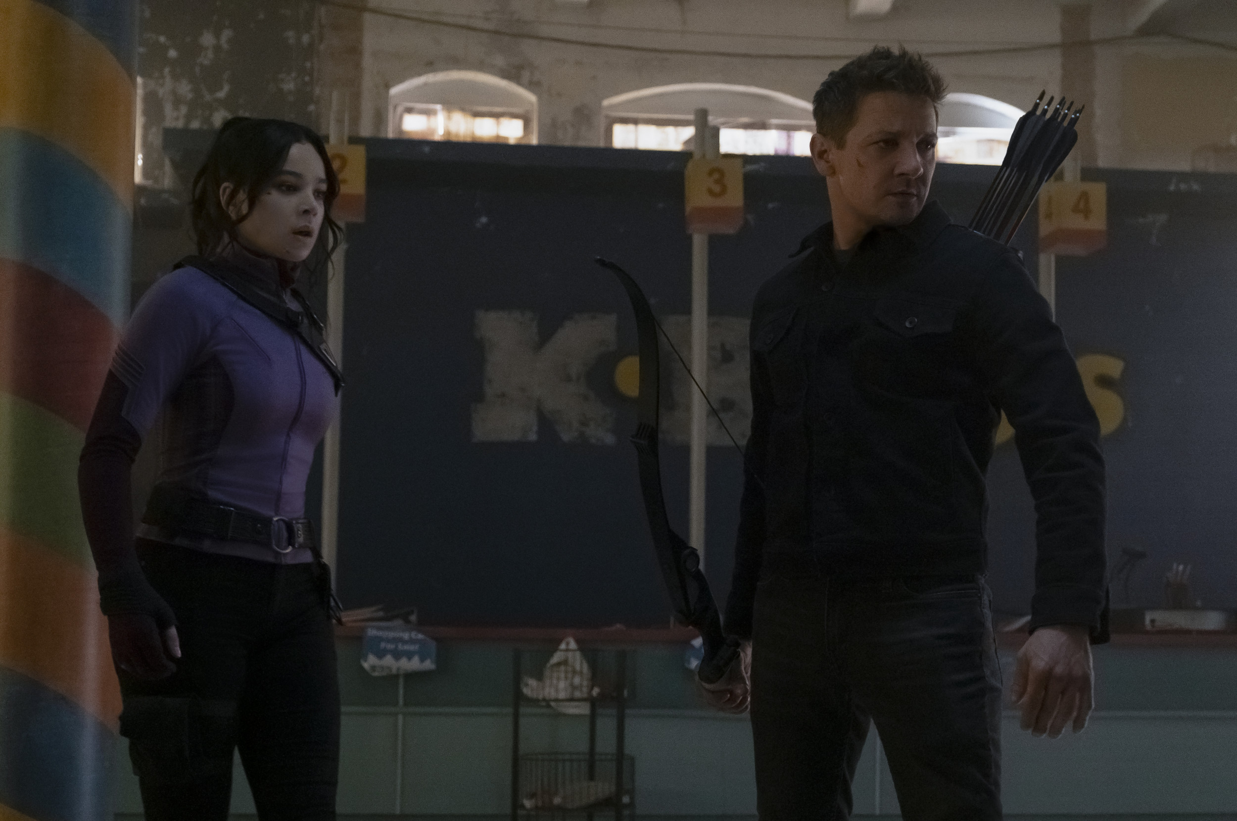 Clint Barton and Kate Bishop in the series Hawkeye. They stand ready to fight in an abandoned toy tore.