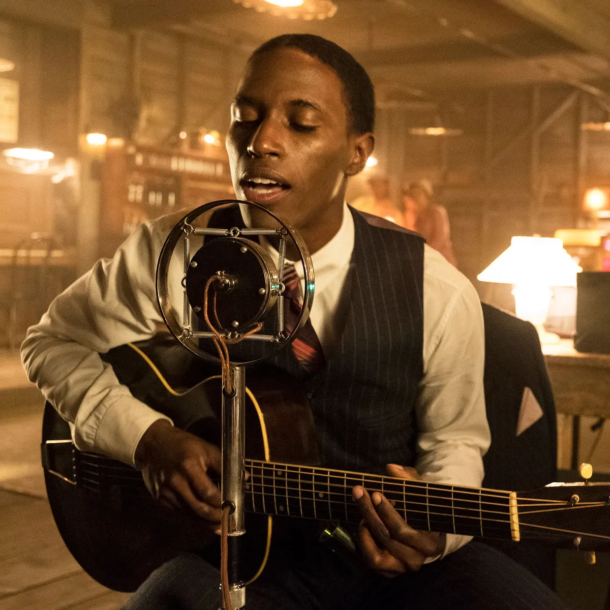 Robert Johnson (Kamahl Naiqui) is singing into an old microphone and playing the guitar.