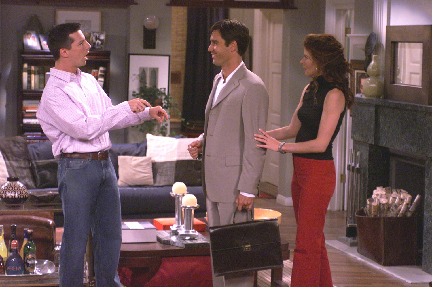 Jack (Sean Hayes) stands in front of Will (Eric McCormack) and points at the ground. Grace (Deborah Messing) stands behind Will with a hand on his arm. Will and Grace. 1998-2020. NBC Universal.