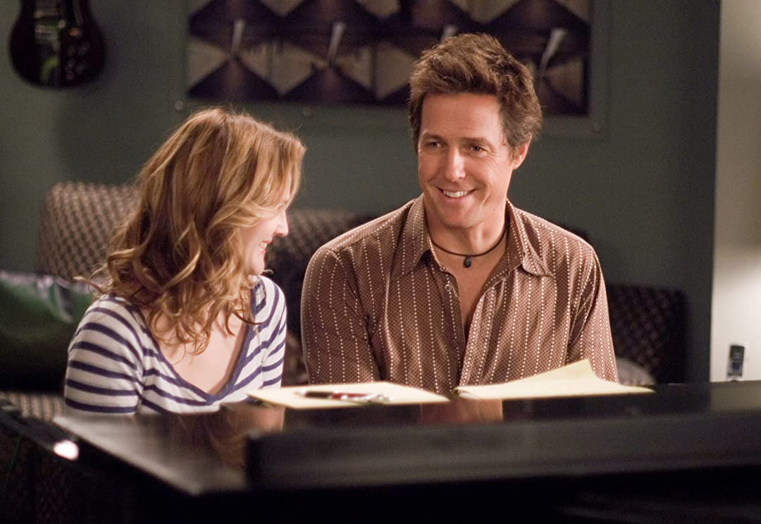 Drew Barrymore as Sophie Fisher and Hugh Grant as Alex Fletcher sitting at the piano together in Music and Lyrics (2007). 