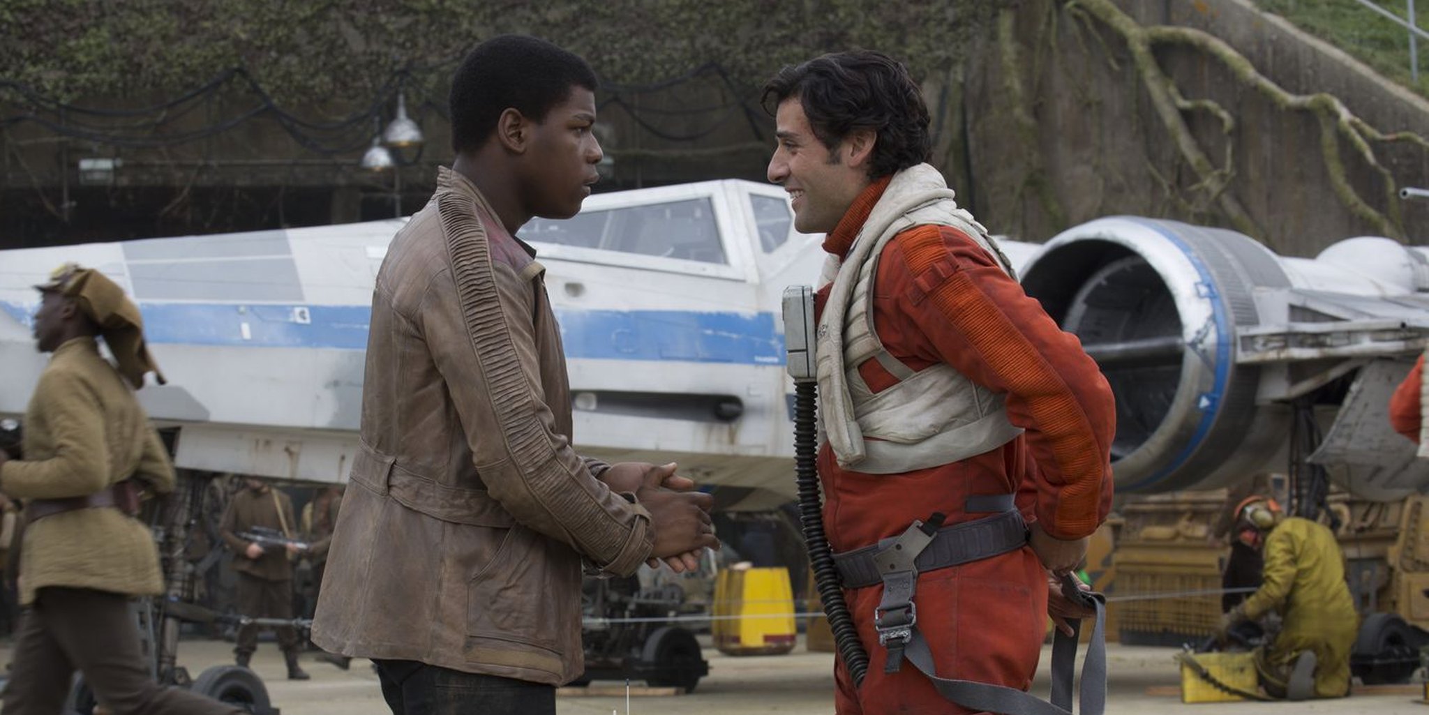 Finn (John Boyega) and Poe Dameron (Oscar Isaac) stand facing each other in front of an aircraft. Finn is wearing a brown leather jacket, Poe is dressed in a resistance pilot's uniform. Abrams, J.J. Dir. Star Wars VII: The Force Awakens. 2015.