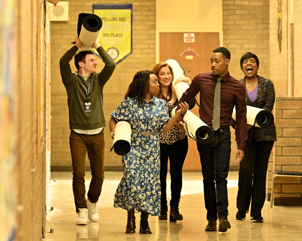 The teachers of 'Abbott Elementary' are walking down a hallway holding new rugs for their students.