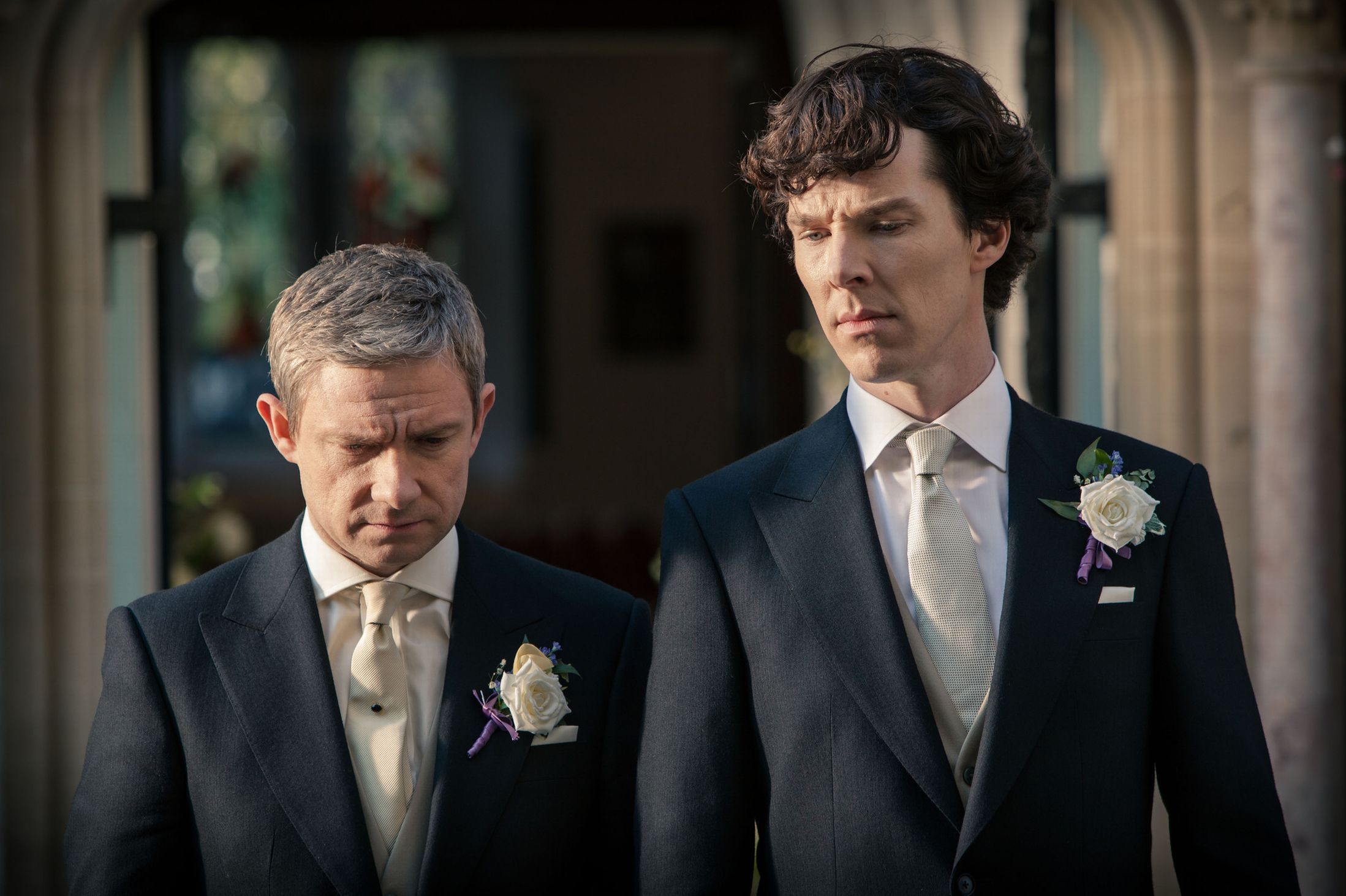 John Watson (Martin Freeman) and Sherlock Holmes (Benedict Cumberbatch) stand next to each other wearing matching suits. They both look concerned. Sherlock. 2010-2017. BBC.