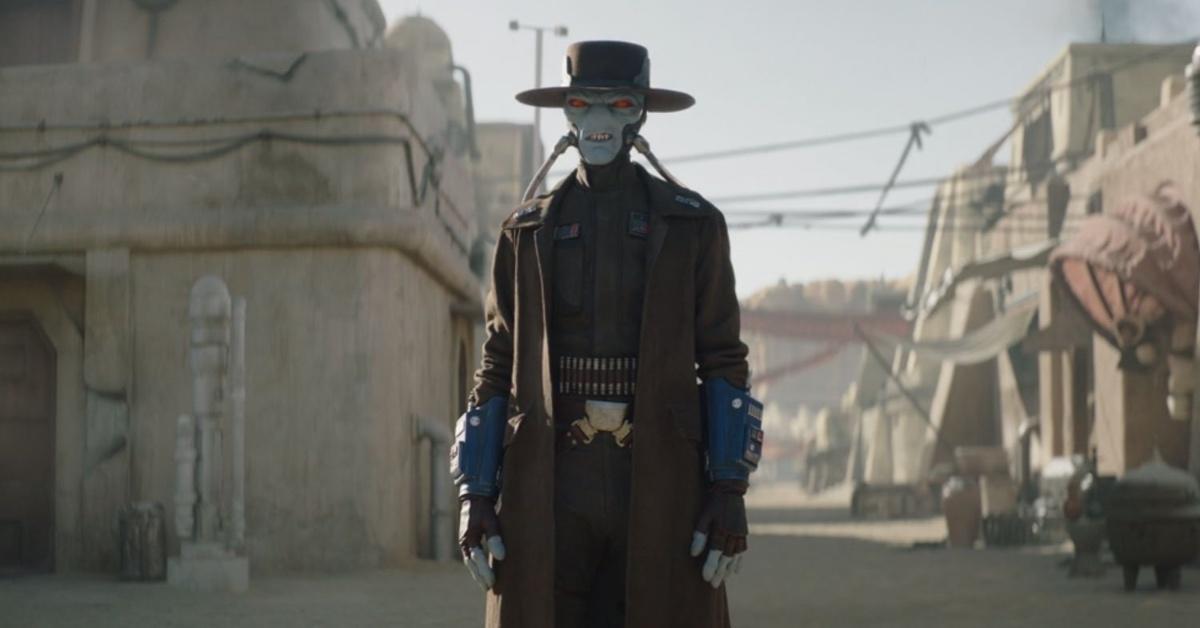 The bounty hunter Cad Bane stands in a street scene. His hands are at his sides. His large red eyes are squinted as he looks on.