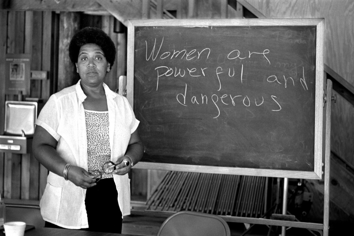 Black and white photo of Audre Lorde standing in front of a blackboard that reads: "Women are powerful and dangerous."