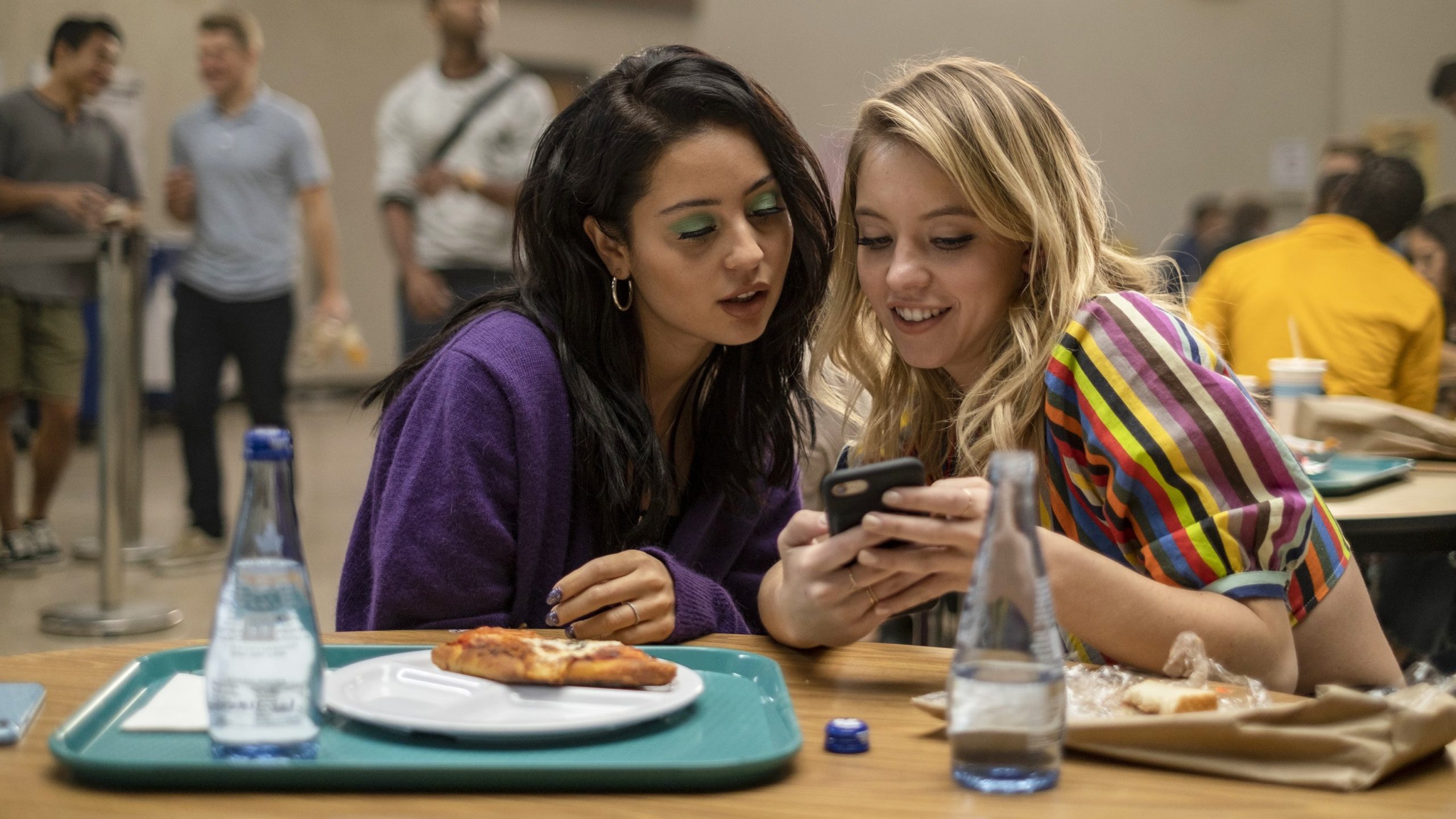 Maddy and Cassie look together at Cassie's phone in the school cafeteria in HBO's 'Euphoria' (2019-).